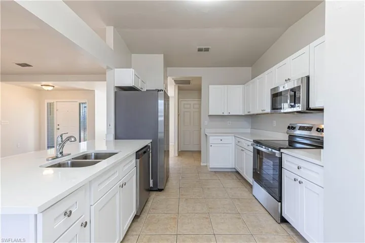 Kitchen with stainless steel appliances, white cabinetry, light tile patterned flooring, light stone countertops, and a peninsula