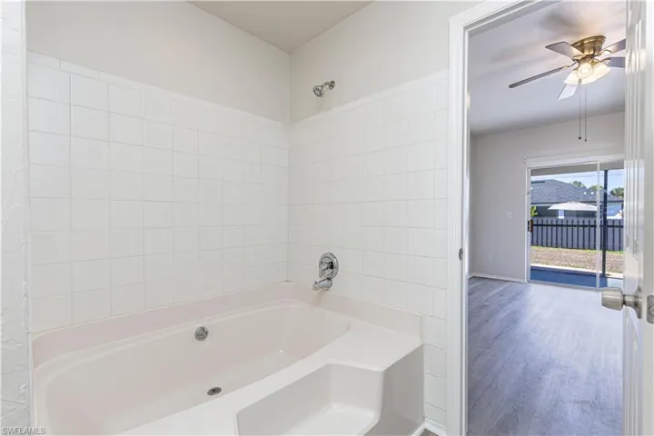Full bath featuring a ceiling fan, wood finished floors, and washtub / shower combination
