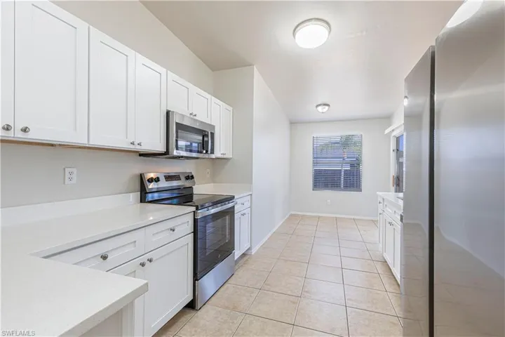 Kitchen with stainless steel appliances, white cabinetry, light tile patterned flooring, and light stone counters