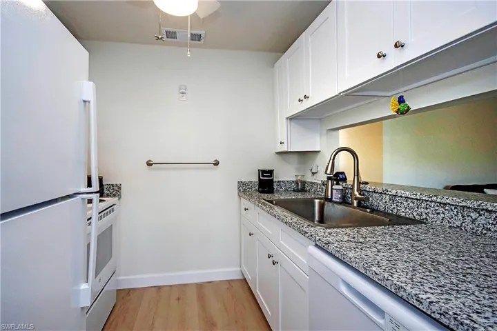 Kitchen with white appliances, light wood-type flooring, white cabinets, stone countertops, and a sink