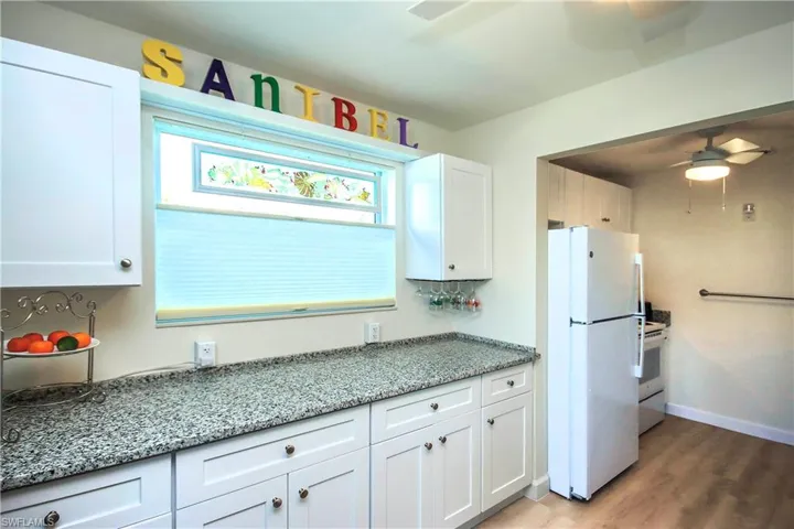 Kitchen with white cabinets, a ceiling fan, white appliances, light stone countertops, and light wood-style flooring