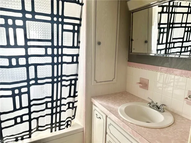 Bathroom featuring shower / bath combo with shower curtain, vanity, and tasteful backsplash