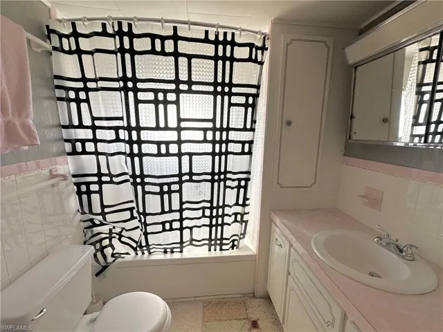 Full bathroom featuring shower / tub combo, tile walls, backsplash, toilet, and vanity