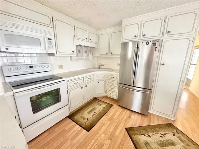 Kitchen with white cabinetry, white appliances, backsplash, light hardwood / wood-style floors, and sink
