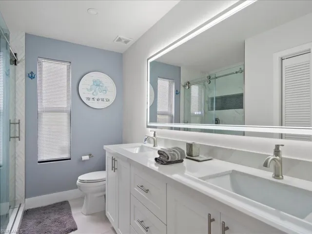 Bathroom with tile patterned flooring, walk in shower, toilet, and dual bowl vanity