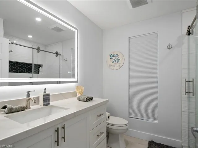 Bathroom with a shower with door, vanity, tile patterned flooring, and toilet