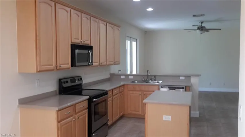 Kitchen with stainless steel electric stove, black microwave, light brown cabinets, light countertops, and a peninsula