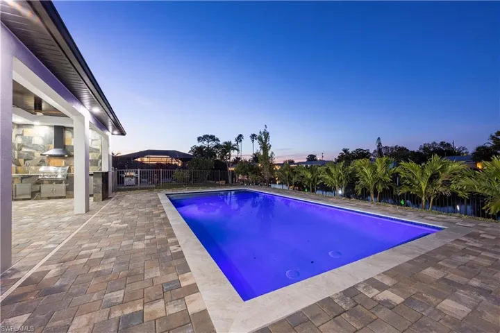 Pool at dusk with area for grilling, grilling area, and a patio