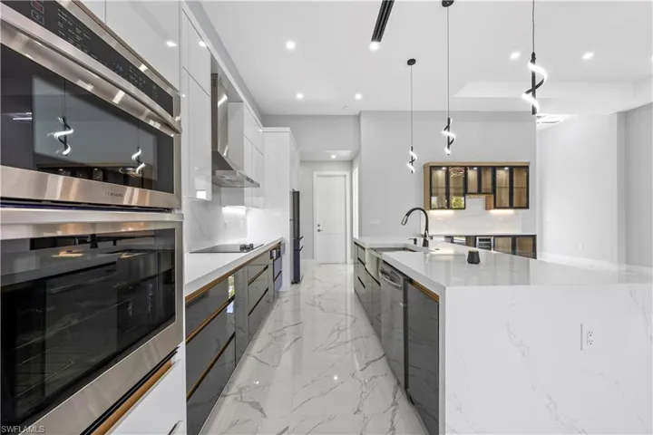 Kitchen featuring white cabinetry, sink, hanging light fixtures, a large island with sink, and stainless steel appliances