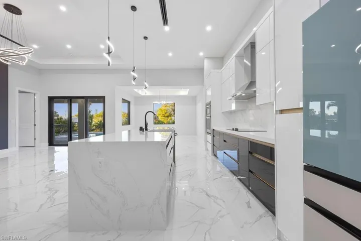 Kitchen with wall chimney exhaust hood, decorative light fixtures, a large island with sink, white cabinets, and backsplash