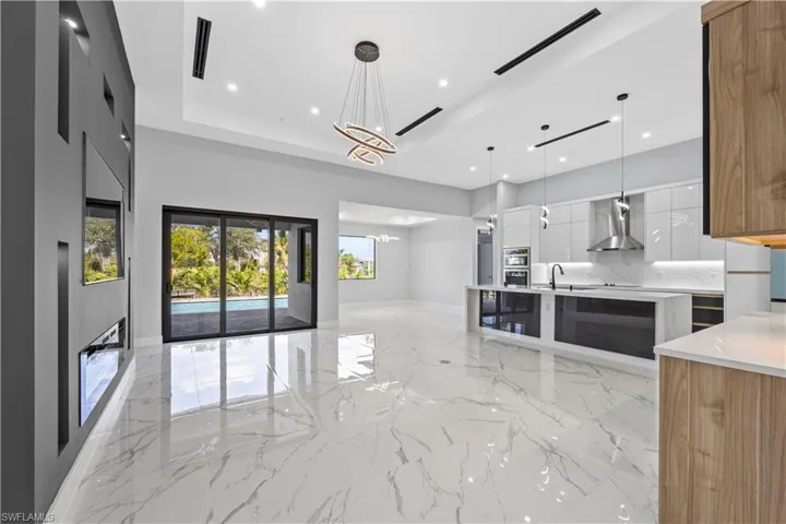Kitchen with white cabinetry, a chandelier, hanging light fixtures, a tray ceiling, and wall chimney exhaust hood