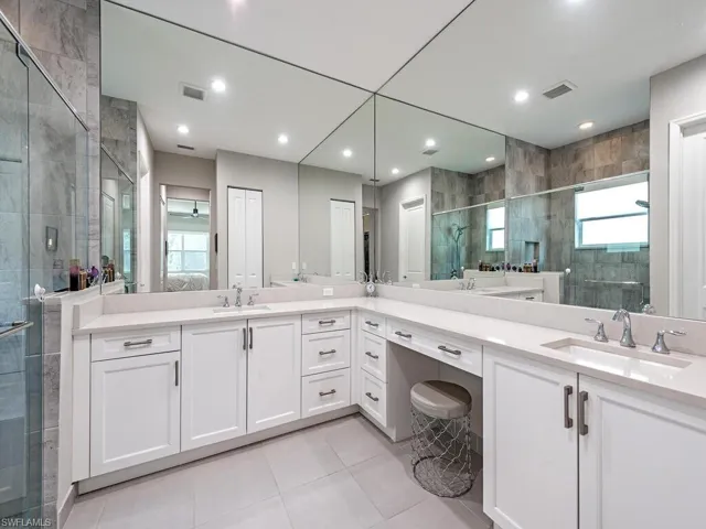 Bathroom featuring a stall shower, two vanities, light tile patterned floors, ensuite bath, and recessed lighting