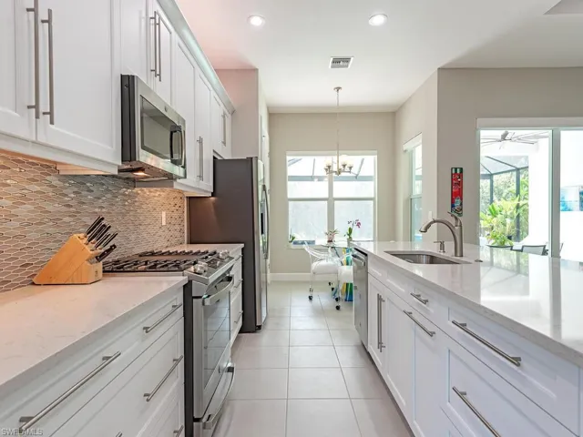 Kitchen with stainless steel appliances, white cabinets, light stone counters, pendant lighting, and light tile patterned floors