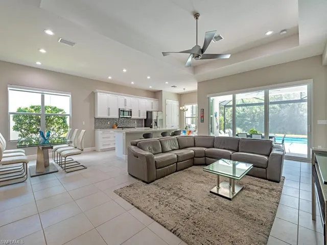 Living room featuring recessed lighting, light tile patterned floors, ceiling fan, a raised ceiling, and a chandelier