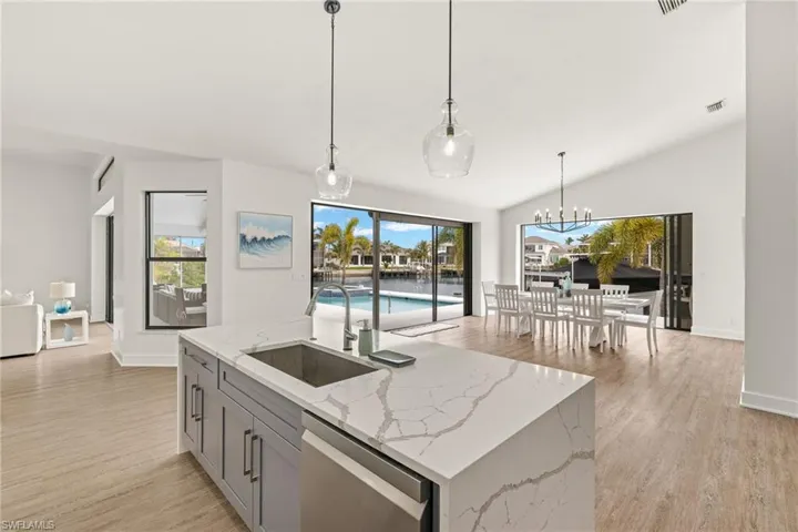 Kitchen with gray cabinetry, sink, stainless steel dishwasher, and light stone countertops