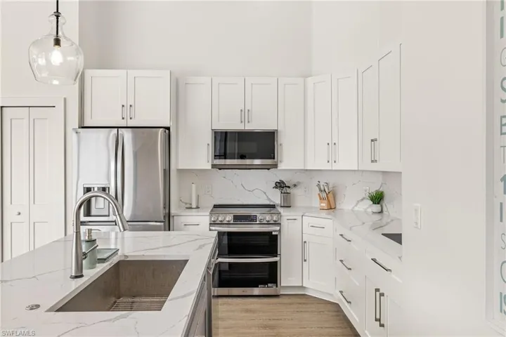 Kitchen featuring pendant lighting, sink, appliances with stainless steel finishes, light stone counters, and decorative backsplash