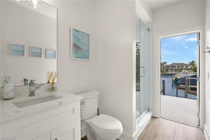 Bathroom with a shower with shower door, wood-type flooring, vanity, toilet, and a water view