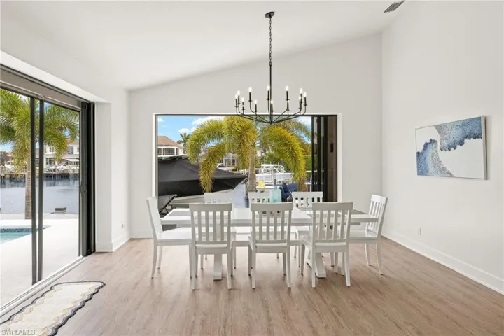 Dining space with vaulted ceiling, a water view, a notable chandelier, and light hardwood / wood-style floors