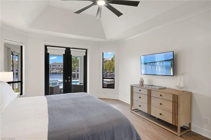 Bedroom with a raised ceiling, hardwood / wood-style floors, access to exterior, and ceiling fan