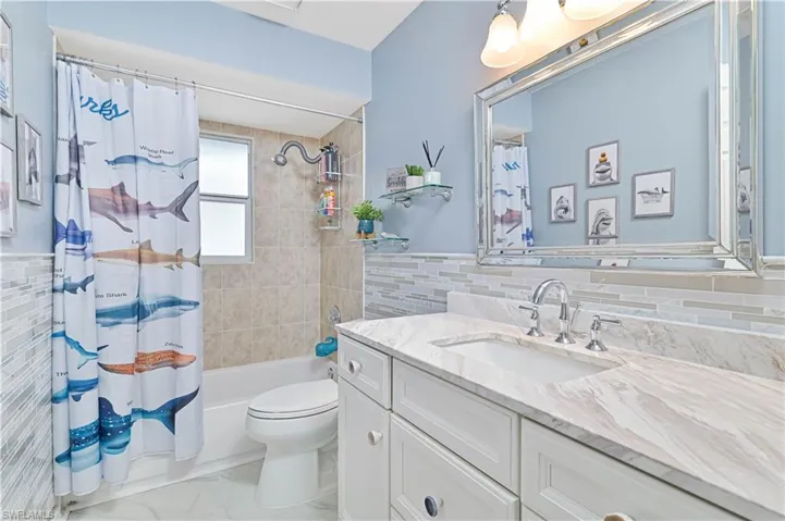 Full bathroom with tile walls, vanity, shower / bathtub combination with curtain, and wainscoting