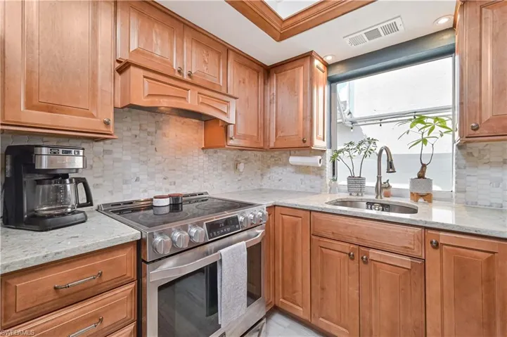 Kitchen with stainless steel electric stove, light stone countertops, and wood finish cabinetry