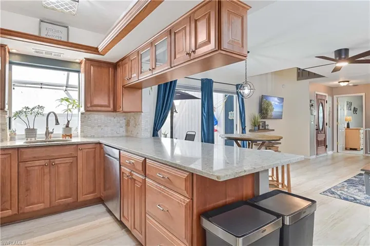 Kitchen with wood finish cabinets, a peninsula, light stone counters, tasteful backsplash, and light wood-style flooring