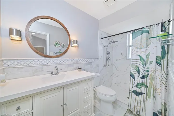 Bathroom with a marble finish shower, vanity, tile walls, and a wainscoted wall