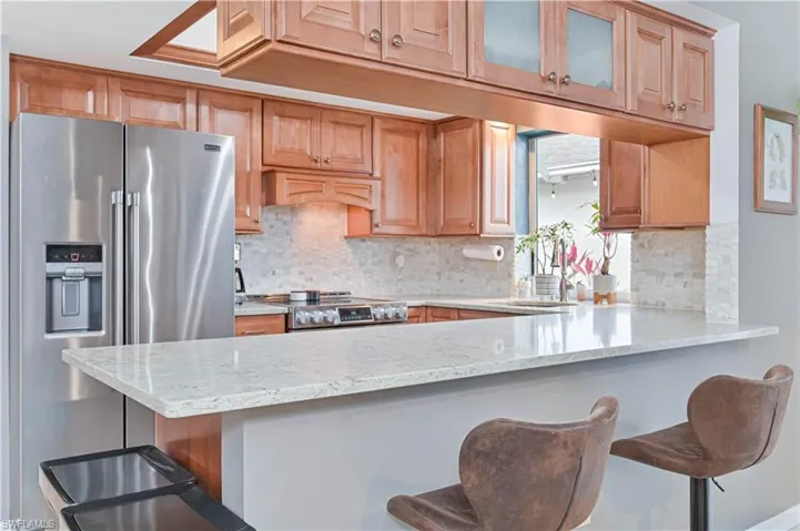 Kitchen featuring stainless steel appliances, a kitchen breakfast bar, a peninsula, light stone counters, and glass insert cabinets
