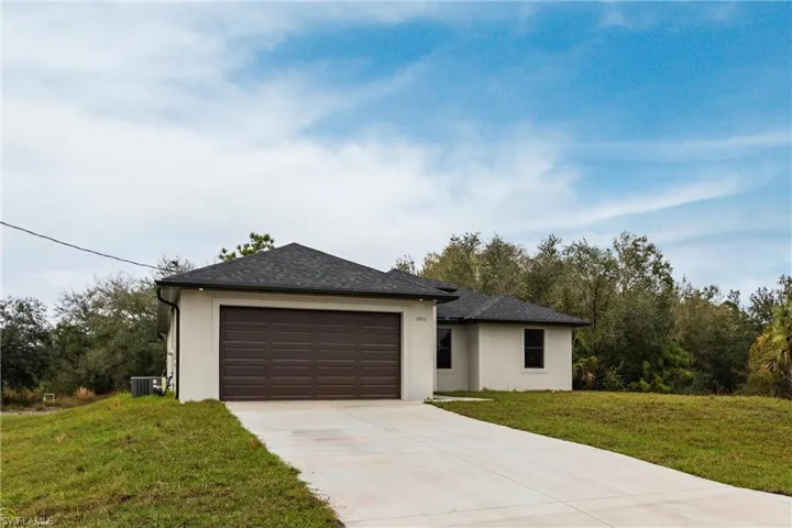View of front of home with a garage, central AC, and a front lawn