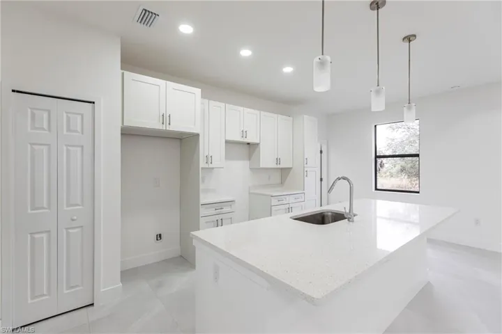 Kitchen with sink, decorative light fixtures, white cabinets, and a center island with sink