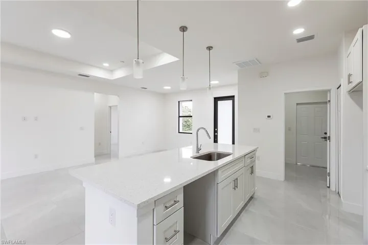 Kitchen featuring decorative light fixtures, white cabinetry, an island with sink, sink, and light stone counters