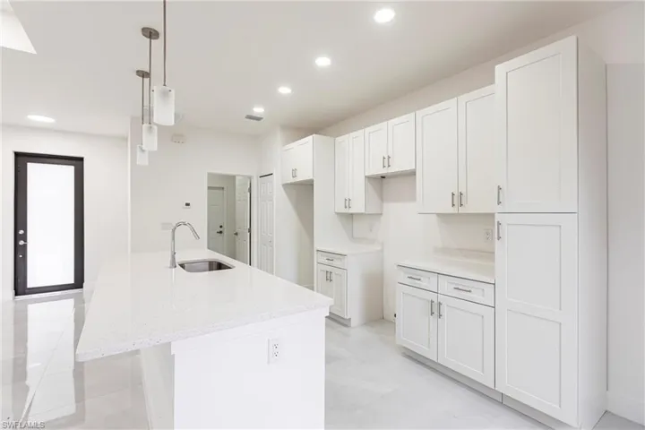 Kitchen featuring sink, a center island with sink, white cabinetry, and hanging light fixtures