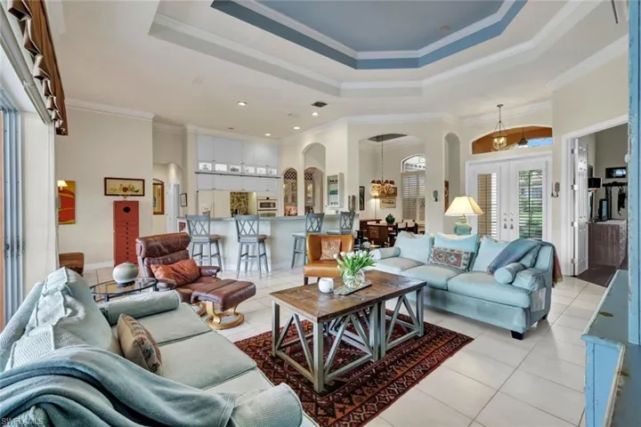 Living room featuring a raised ceiling, crown molding, french doors, and light tile patterned floors
