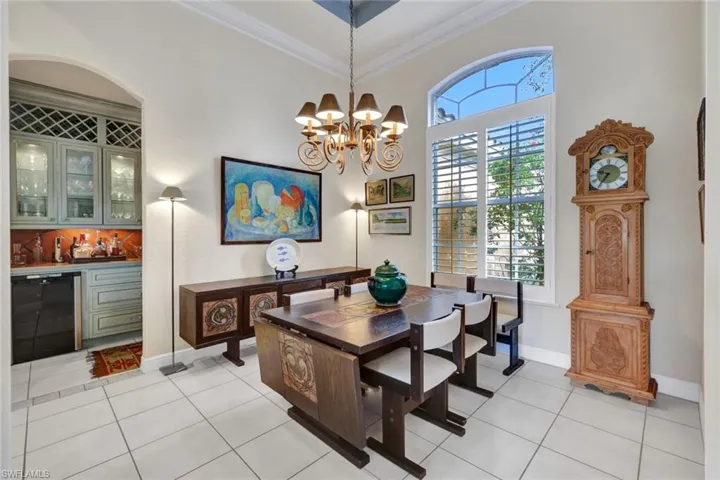 Tiled dining room featuring ornamental molding, indoor bar, a towering ceiling, and a chandelier