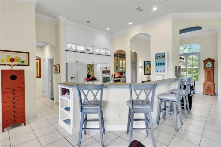 Kitchen with kitchen peninsula, white cabinetry, ornamental molding, and a breakfast bar area