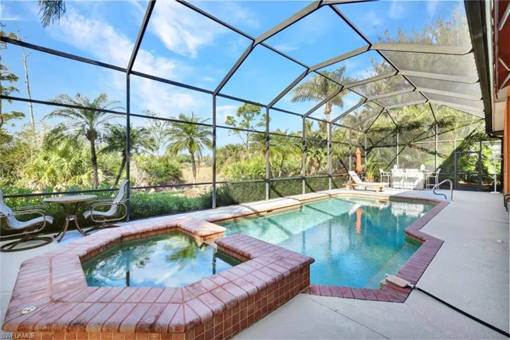View of pool featuring glass enclosure, a patio area, and an in ground hot tub