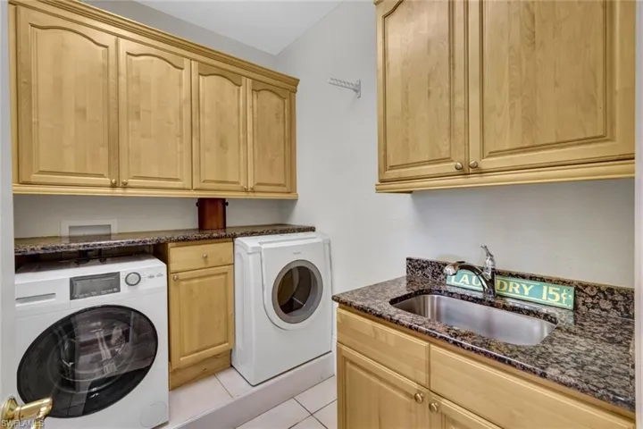 Clothes washing area with cabinets, light tile patterned floors, washing machine and dryer, and sink