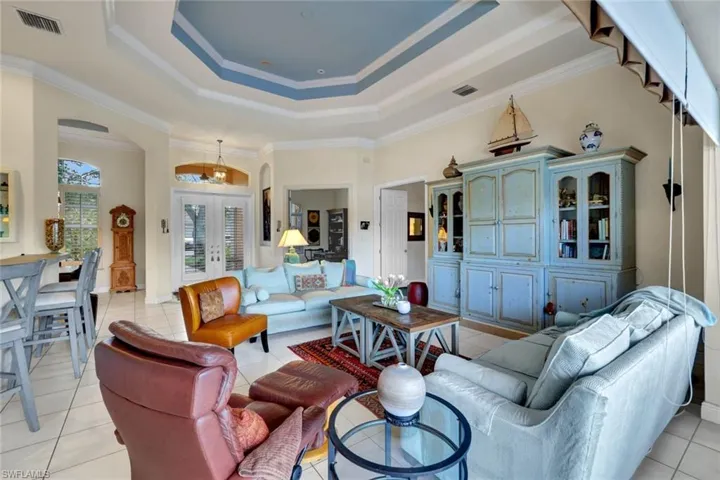 Tiled living room featuring french doors, a raised ceiling, and ornamental molding