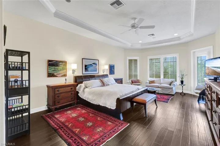 Bedroom with ceiling fan, dark hardwood / wood-style flooring, ornamental molding, and a tray ceiling