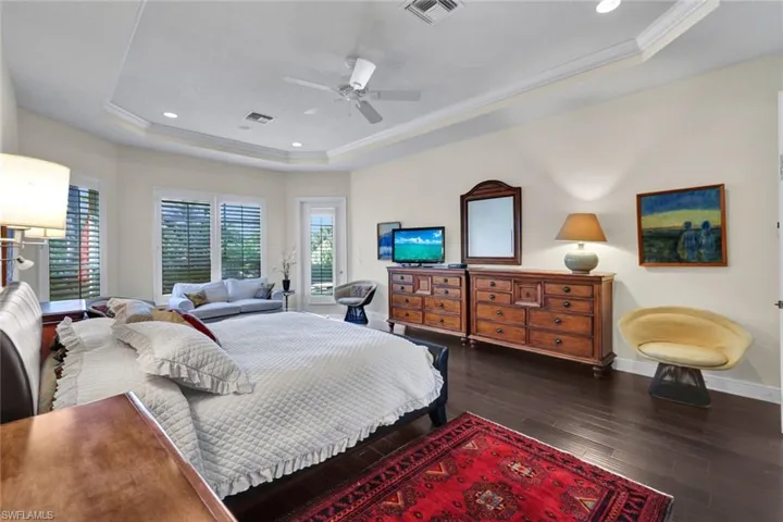 Bedroom featuring ornamental molding, a raised ceiling, ceiling fan, and dark wood-type flooring