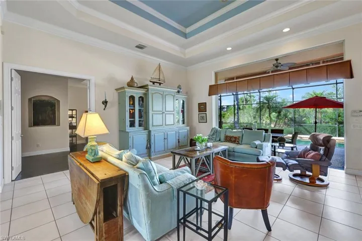 Tiled living room with a tray ceiling, ceiling fan, and ornamental molding