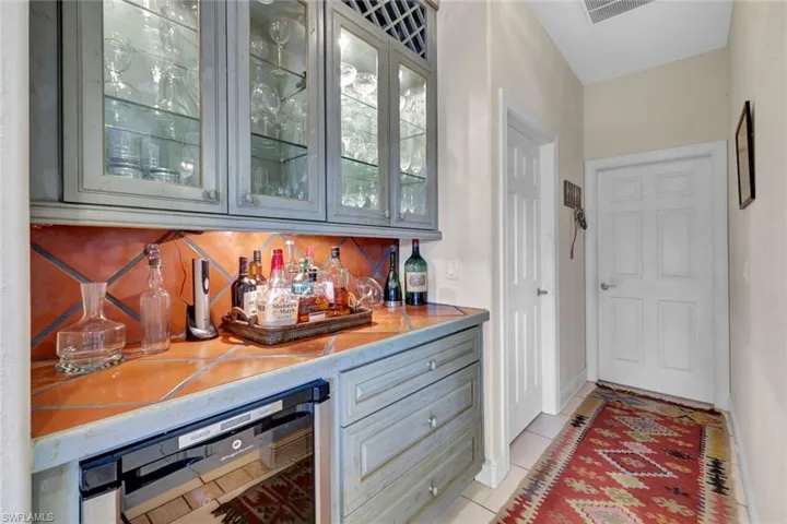 Bar with light tile patterned floors, tasteful backsplash, and beverage cooler