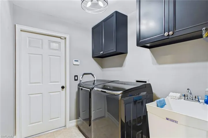 Dedicated utility space featuring overhead dark cabinetry, a white six-panel door, and a built-in utility sink with a chrome faucet