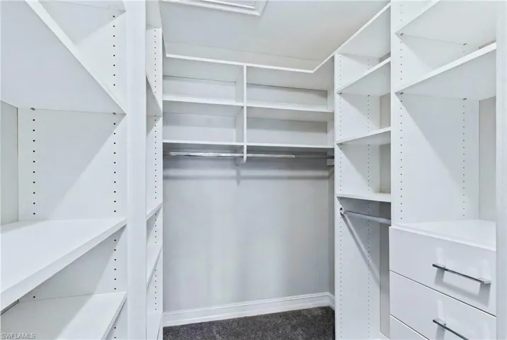 Walk-in closet featuring white built-in shelving, multiple hanging rods, and integrated drawers with silver-tone hardware
