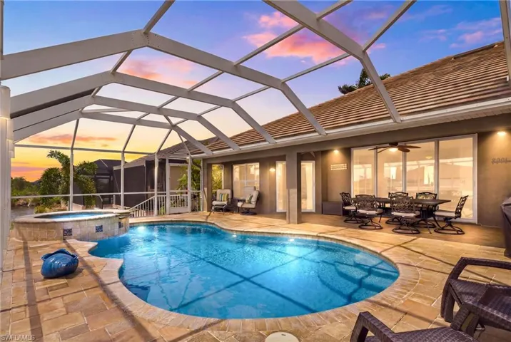 Screened lanai featuring a freeform pool, integrated spa with tile accents, and paver decking