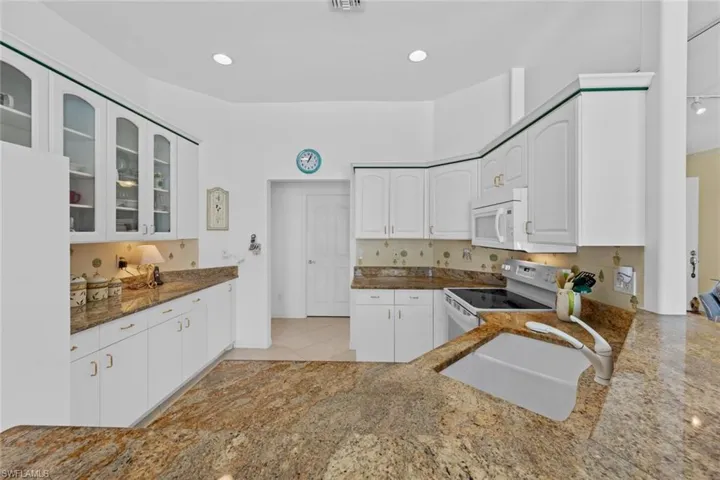 Kitchen with white cabinets, white appliances, kitchen peninsula, and sink