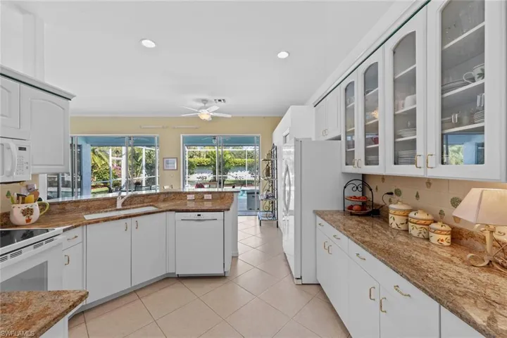 Kitchen featuring ceiling fan, sink, light stone countertops, white appliances, and white cabinets
