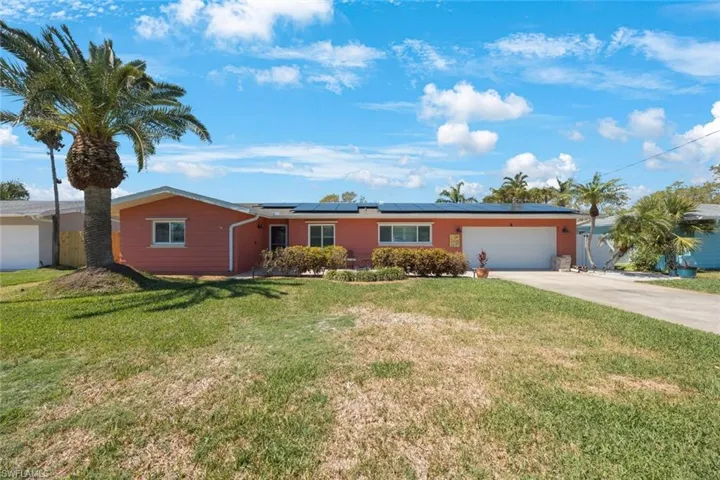 Single story home featuring a front yard, concrete driveway, a garage, and roof mounted solar panels