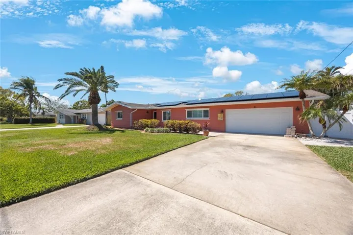 Ranch-style house featuring an attached garage, solar panels, concrete driveway, and a front yard