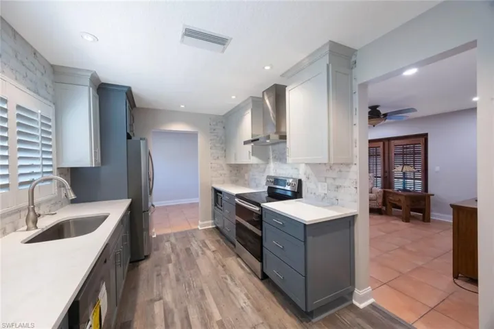 Kitchen featuring visible vents, a sink, wall chimney range hood, appliances with stainless steel finishes, and light countertops